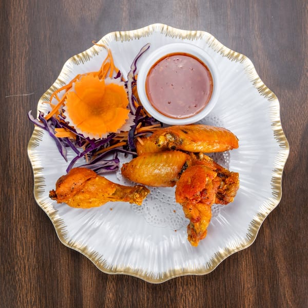 Golden fried chicken wings and drumsticks with a side of dipping sauce and shredded vegetables.