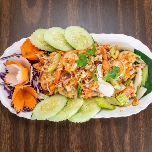 Thai glass noodle salad with shrimp, ground chicken, vegetables, and peanuts, garnished with cucumber slices.