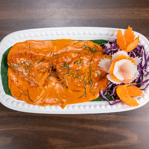 Red curry dish with kaffir lime leaves, garnished with shredded cabbage and carrot carvings.