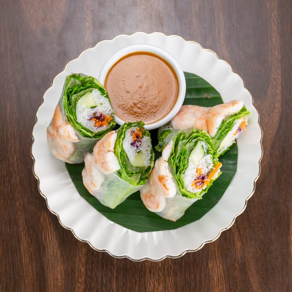 Four fresh shrimp spring rolls with lettuce, rice, and vegetables, served with peanut sauce.