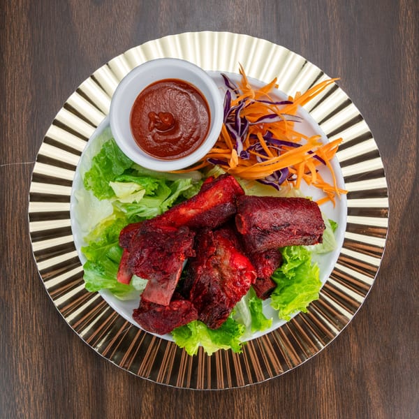 Red marinated ribs on a bed of lettuce with shredded carrots, cabbage, and a side of sauce.