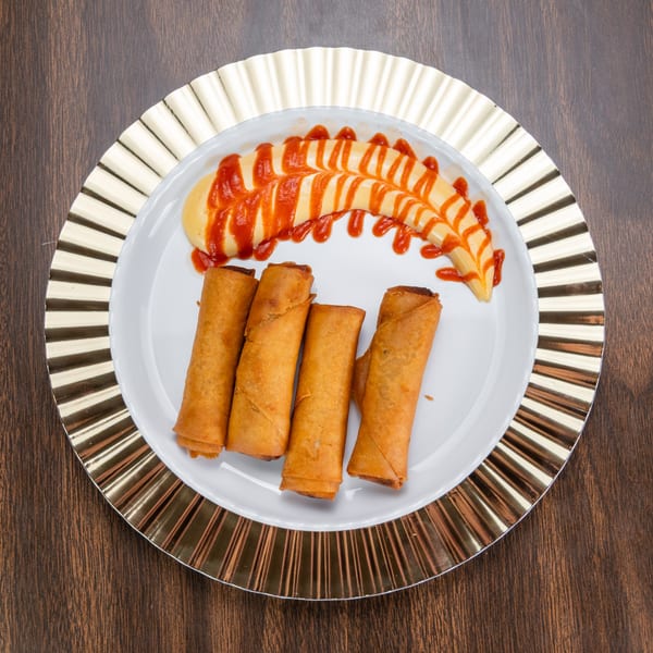 Four crispy spring rolls on a white plate with a side of yellow sauce drizzled with red sauce.