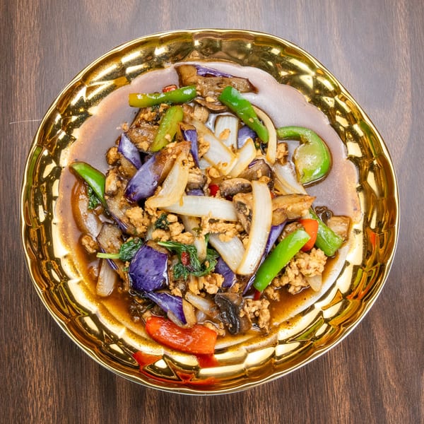 Stir-fried eggplant, ground meat, onions, and peppers in a rich sauce on a gold plate.