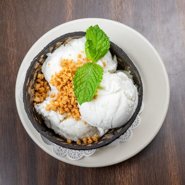 Coconut ice cream with crushed peanuts and mint leaves, served in a coconut shell bowl.
