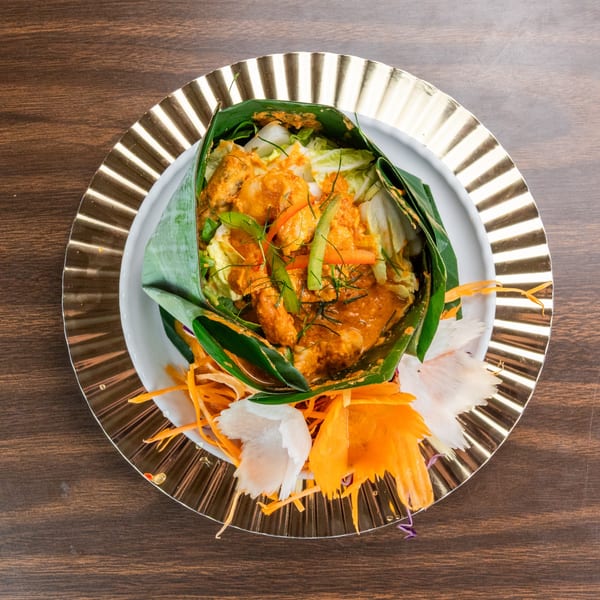 Curry chicken and vegetables wrapped in a banana leaf, garnished with shredded carrots and radish.