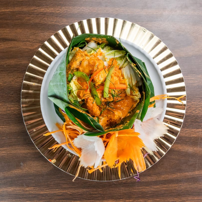 Curry chicken and vegetables wrapped in a banana leaf, garnished with shredded carrots and radish.